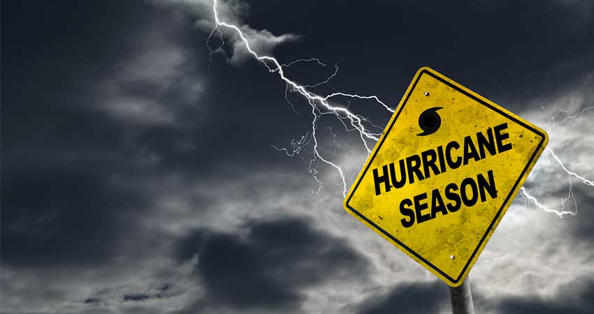 Hurricane season warning sign in front of approaching storm clouds, symbolizing the need for timely alerts and emergency preparedness.